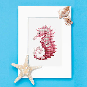 Diamond painting of a pink seahorse in a white frame, decorated with seashells and a starfish, promoting Mini Kunst artwork.