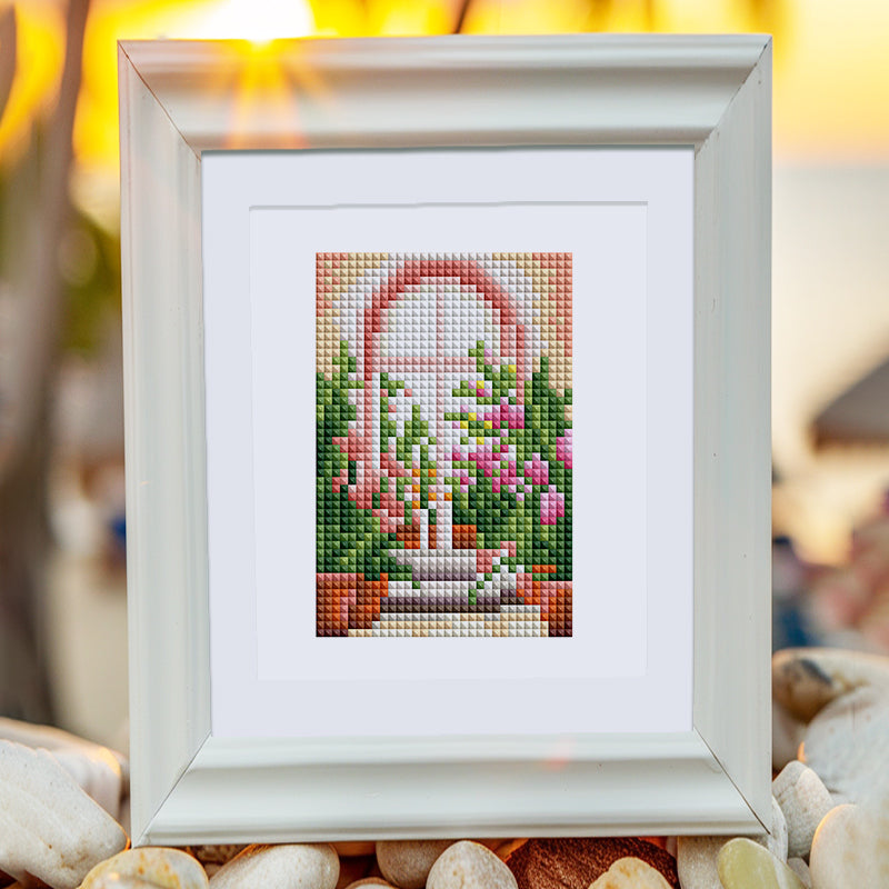 Framed diamond painting artwork of a vibrant garden with flowers and archway displayed outdoors during sunset. Mini Kunst set.