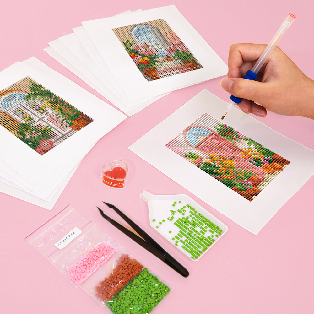 Person working on Willkommen Zwei 12er SET - Diamond Painting with various tools and colorful mini art designs on pink background.