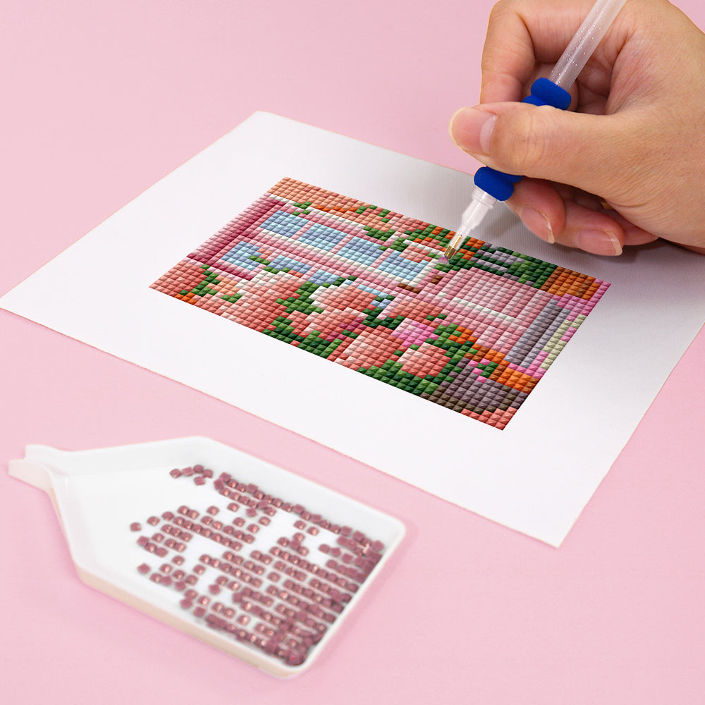 Hand creating Mini Kunst with Diamond Painting, showcasing intricate designs and vibrant colors on a pink background.