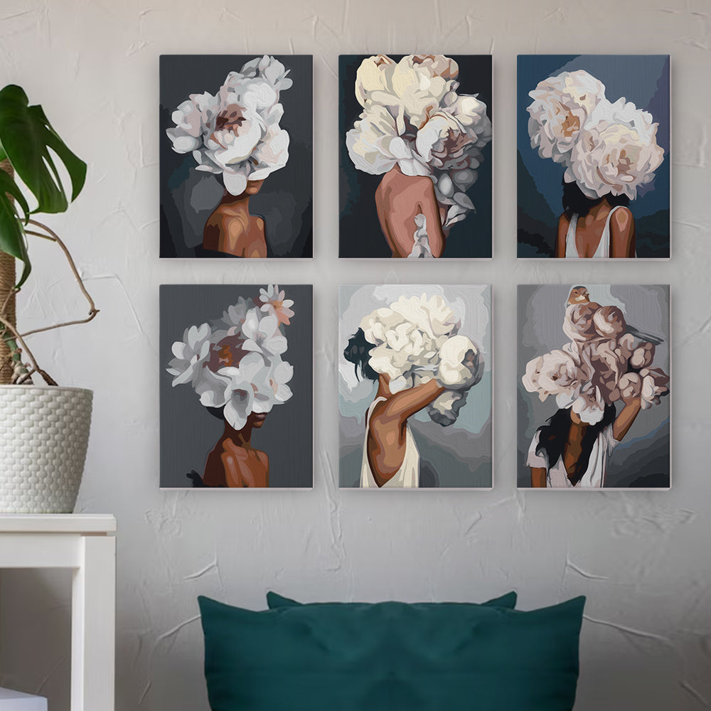 Six canvas paintings of individuals with flower-adorned hair, displayed on a wall with a plant and seating in the foreground