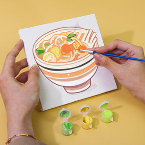 Person painting a bowl of noodles on a canvas with small acrylic paint pots displayed, part of Küchen Edition Zwei 6er SET, Malen nach Zahlen.