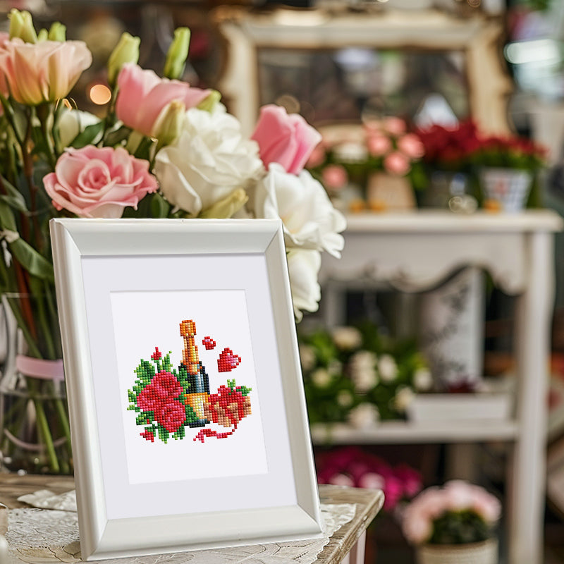 Framed diamond painting of flowers and champagne displayed among floral arrangements.